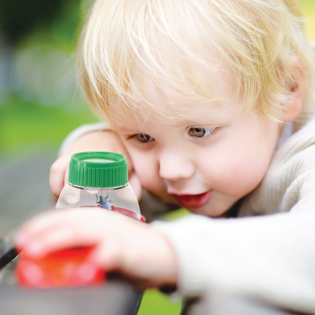 Cute toddler boy playing with toy cars outdoors at warm summer day